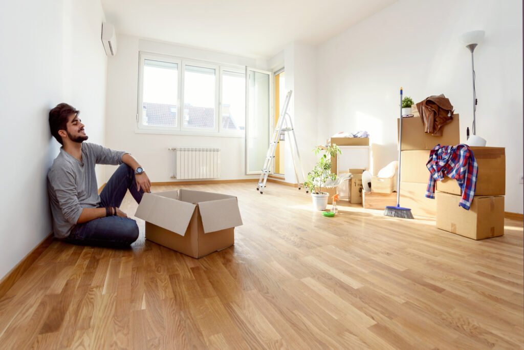 Happy young man just moved into new home unpacking boxes sitting on the floor